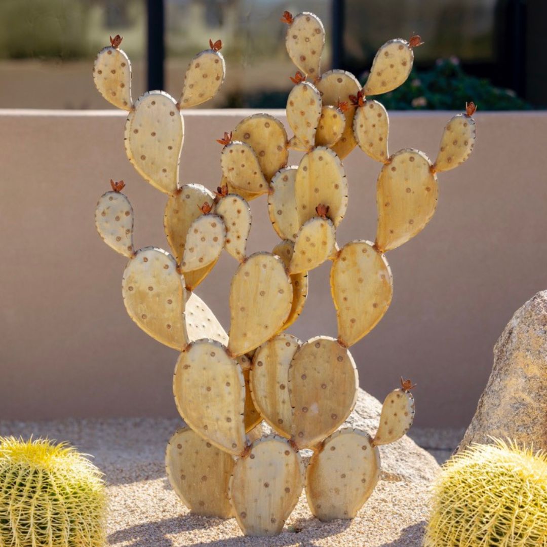 A handcrafted realistic large metal prickly pear cactus planted into gravel in a yard. Two real cactus' can be seen either side.