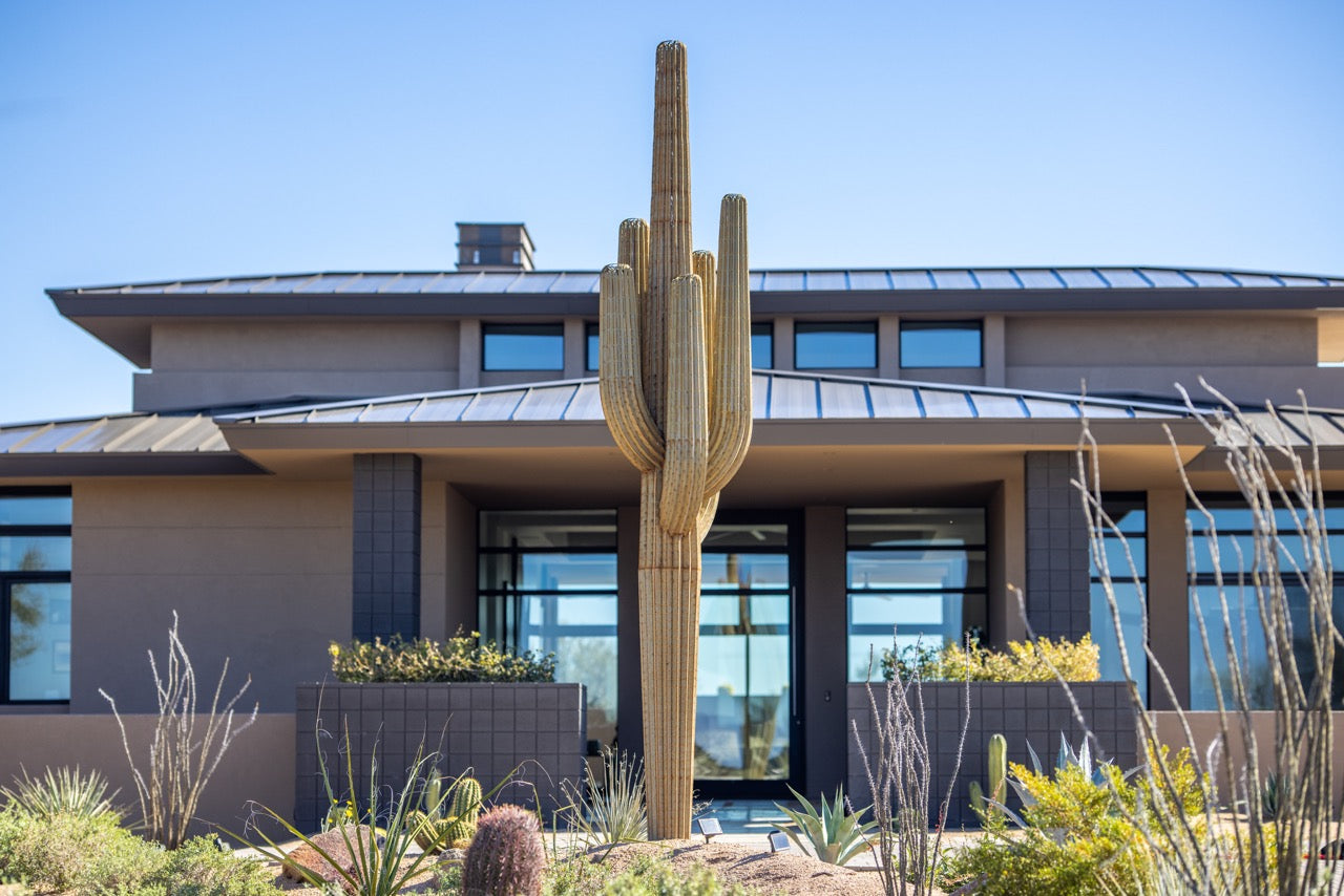 A handcrafted realistic 17ft metal saguaro cactus outside in the front yard. House pictured on background.