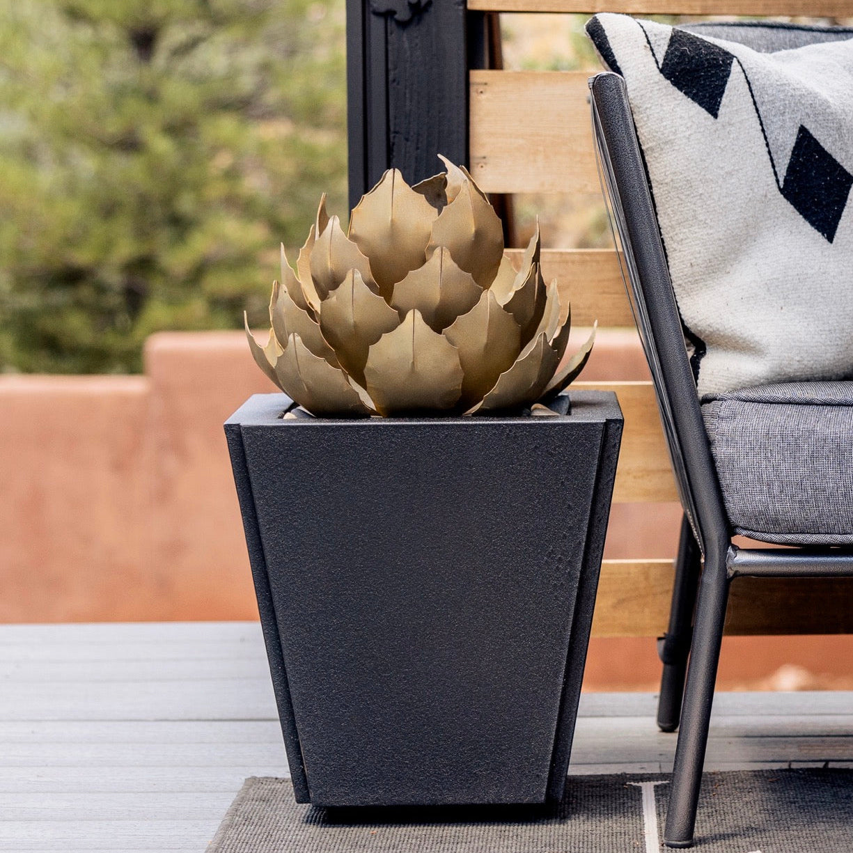 Decorative agave in a black pot on a table with outdoor furniture in the background