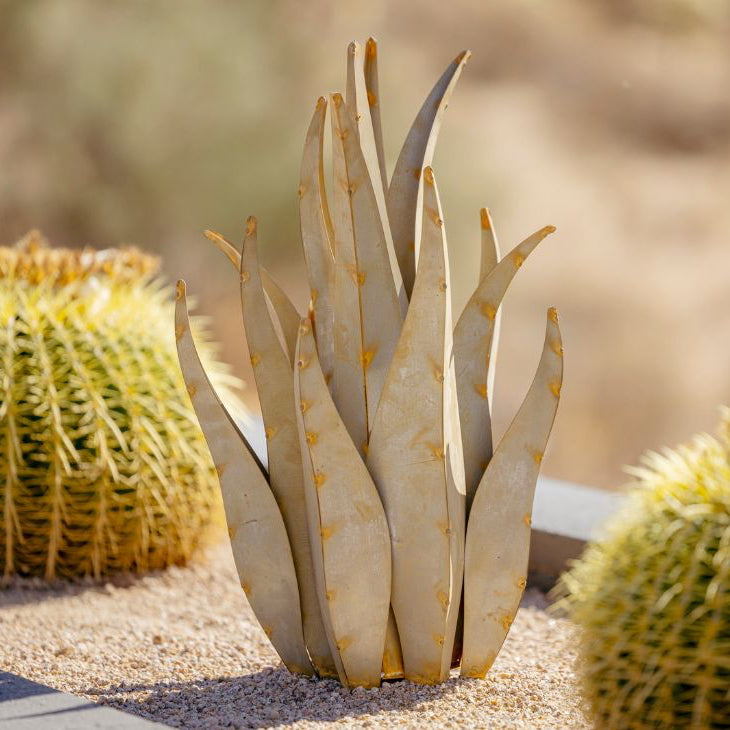 A handcrafted metallic sculpture resembling an agave plant, with a desert landscape in the background.