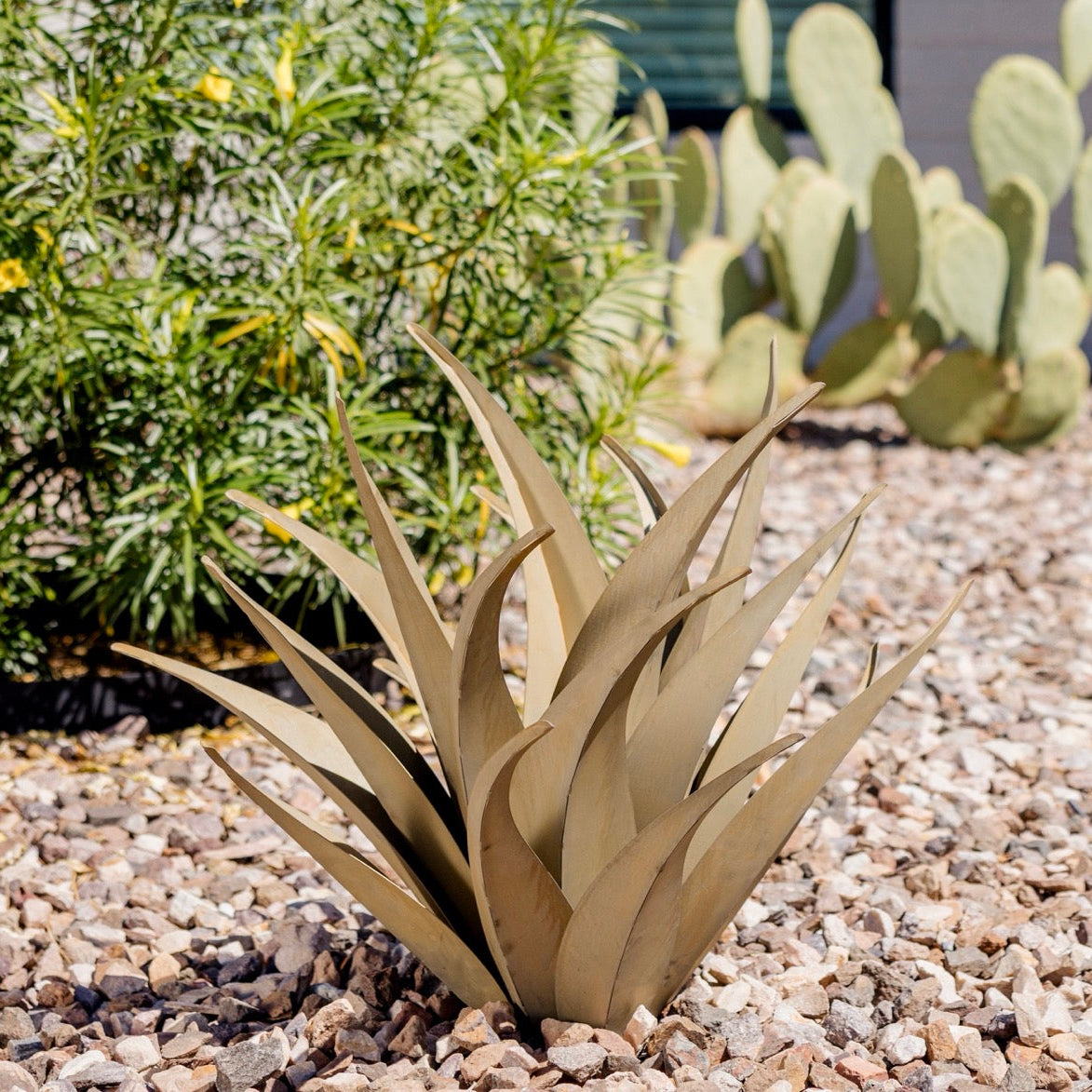 Metallic aloe vera plant sculpture on a gravel surface with cacti in the background