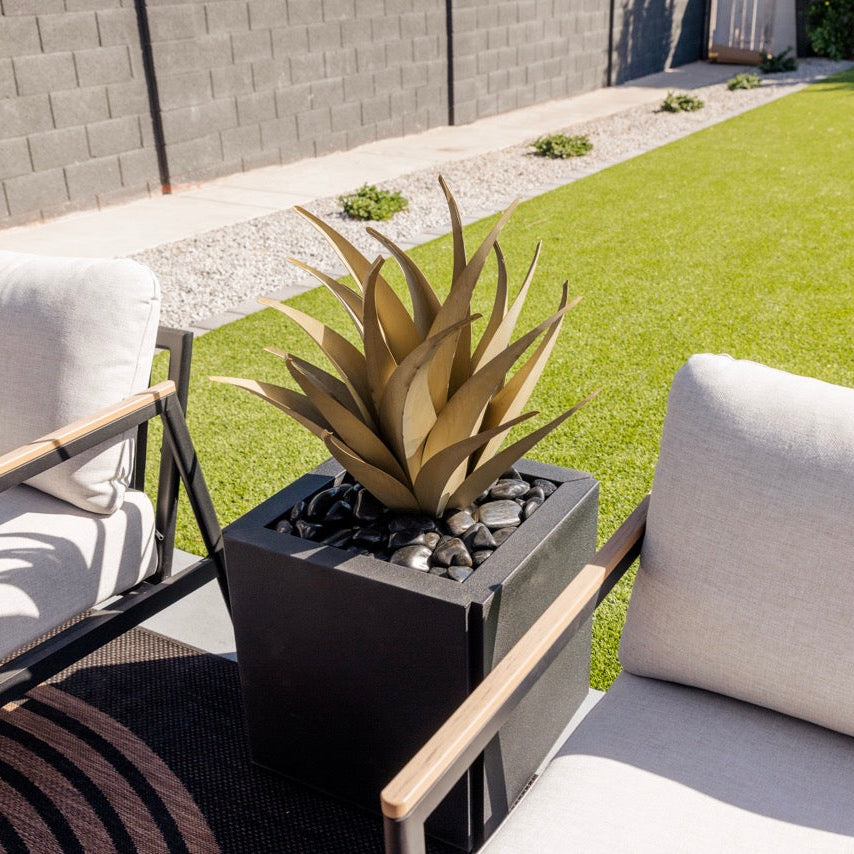 Outdoor patio with a potted steel agave between two chairs on a grassy area.