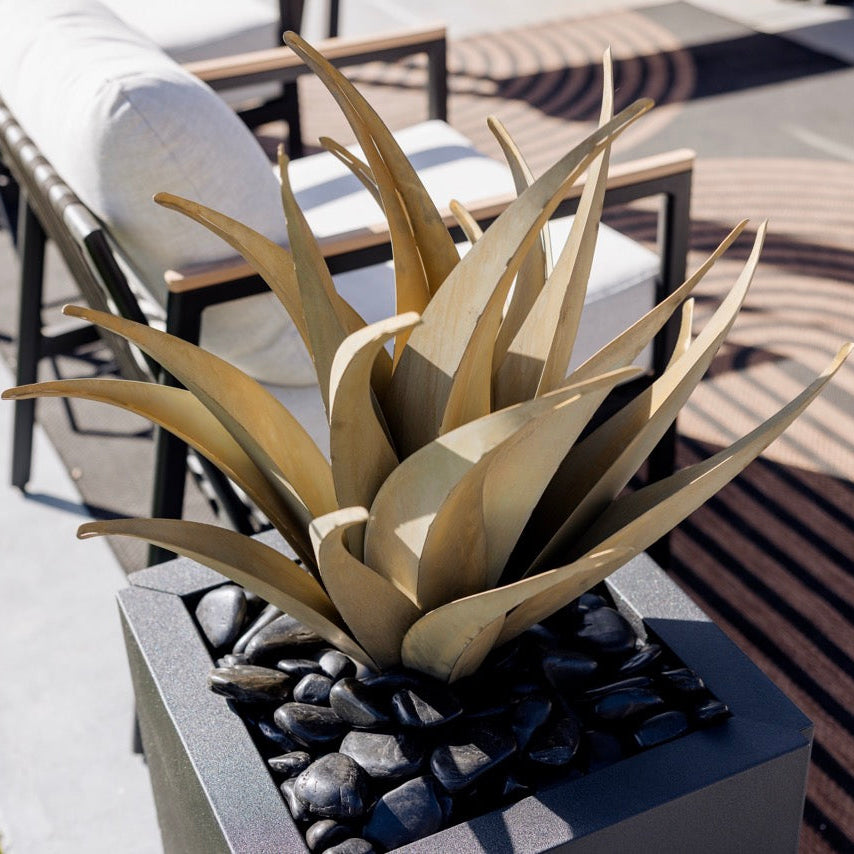 Decorative steel agave in a pot on a patio with lounge chairs in the background