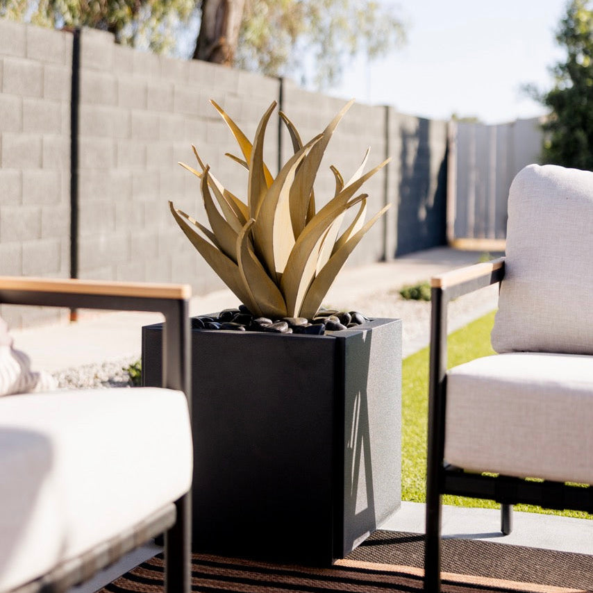 Outdoor patio with black planter, white cushioned chairs, and trees in the background