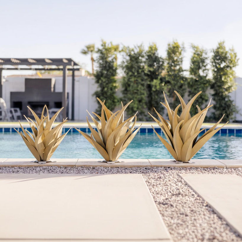 Decorative steel agaves in front of a pool with trees and a building in the background