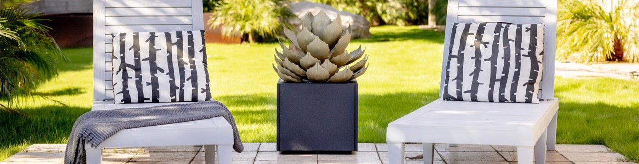 Two white lounge chairs with patterned cushions on a patio area with a potted plant in the background.