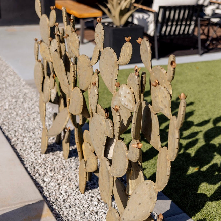 Decorative cactus sculpture on a gravel path with outdoor furniture in the background