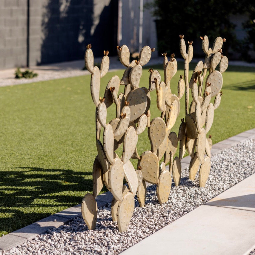 Decorative stone cacti sculpture on a gravel bed with grass and a wall in the background
