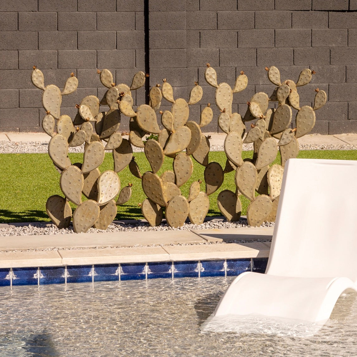 Decorative cactus wall art in front of a pool with a white lounge chair.