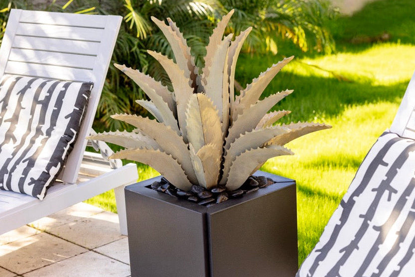 Two white lounge chairs with patterned cushions and a steel agave in a planter on a patio.