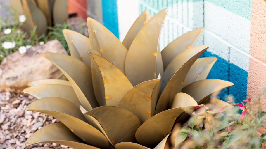 Gold-colored steel agave plant against a colorful outdoor background