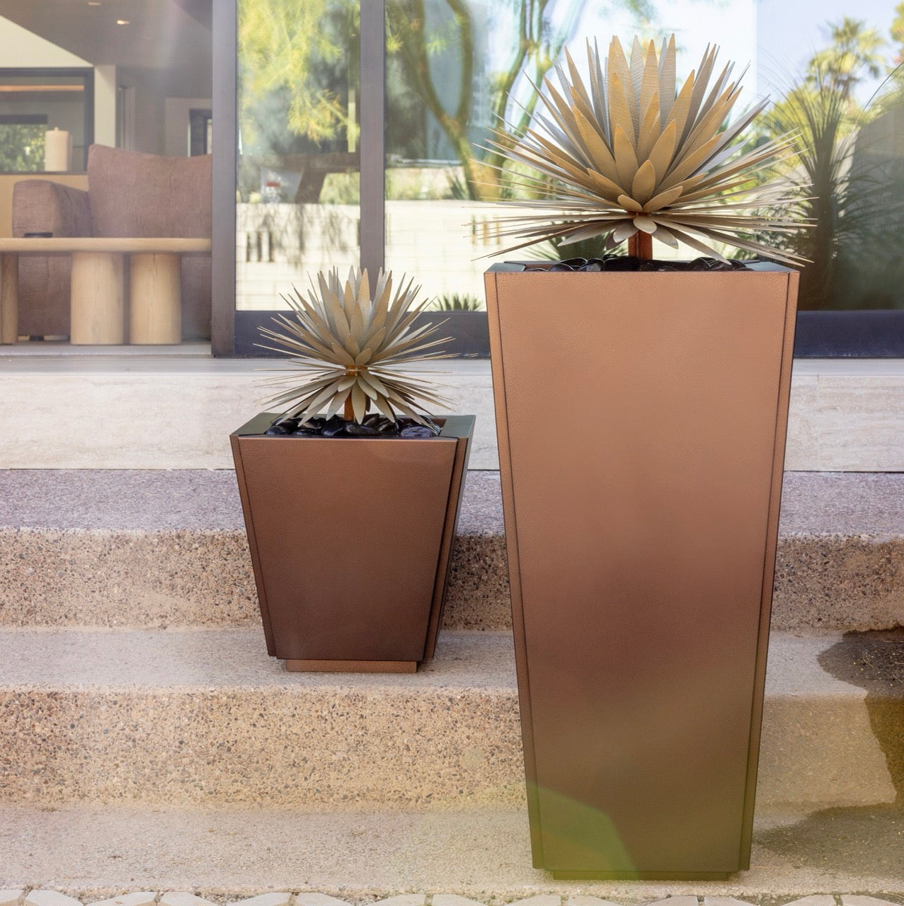 Two tall bronze steel planters with spiky steel plants on a patio.
