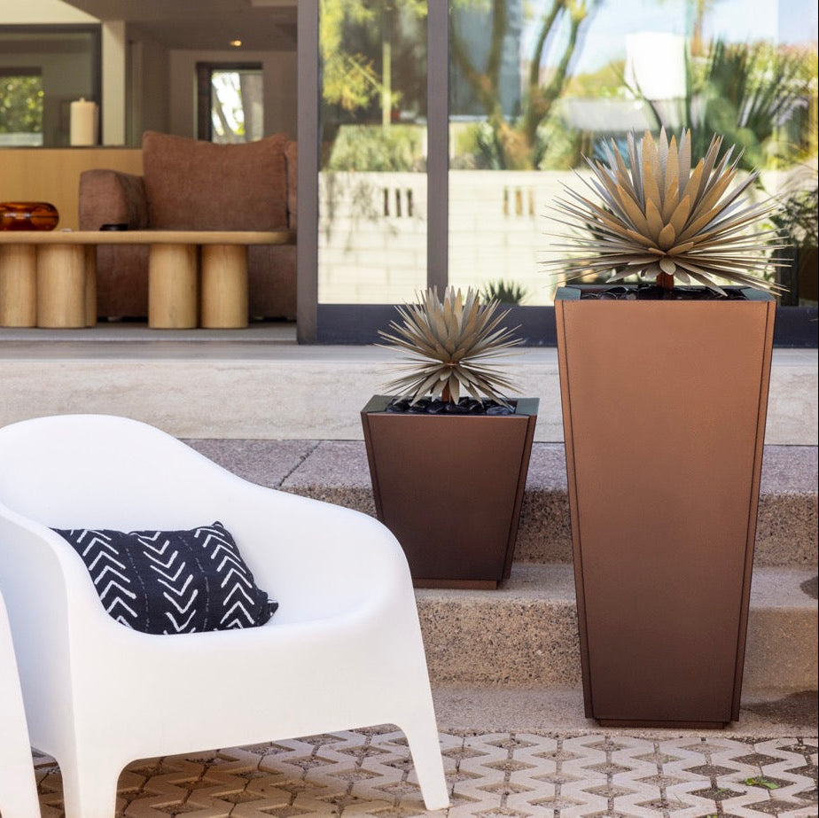 Outdoor seating area with white chairs, black and white patterned pillows, and large planters.