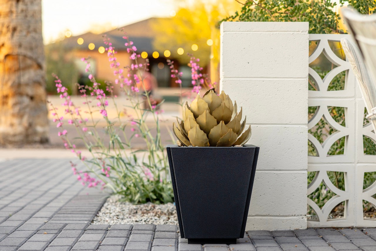 A medium handcrafted metal artichoke agave sculpture inside a black planter, located on the front yard.