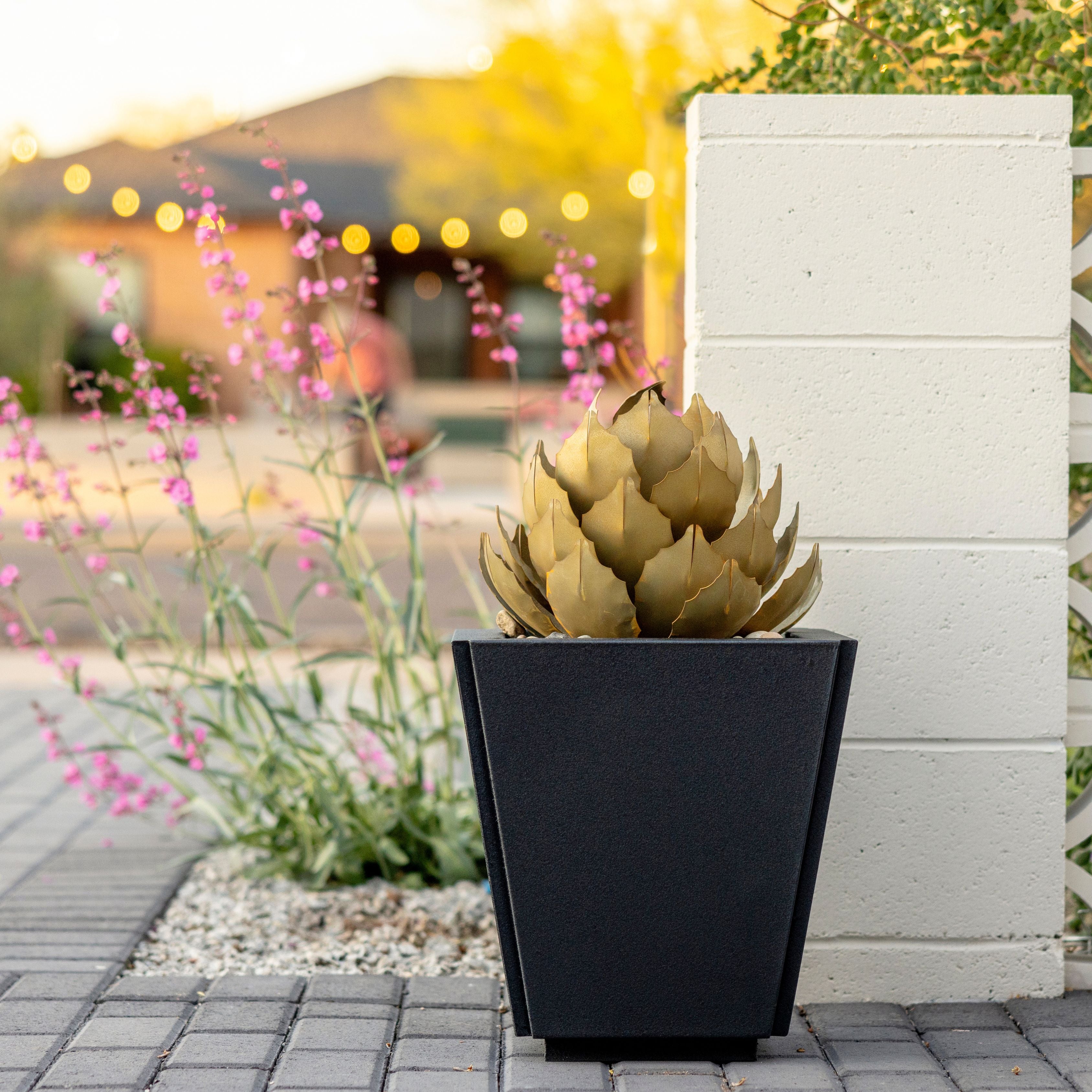 A medium size metal artichoke sculpture that is displayed in a graphite parks planter. Featuring a residential driveway in the background.