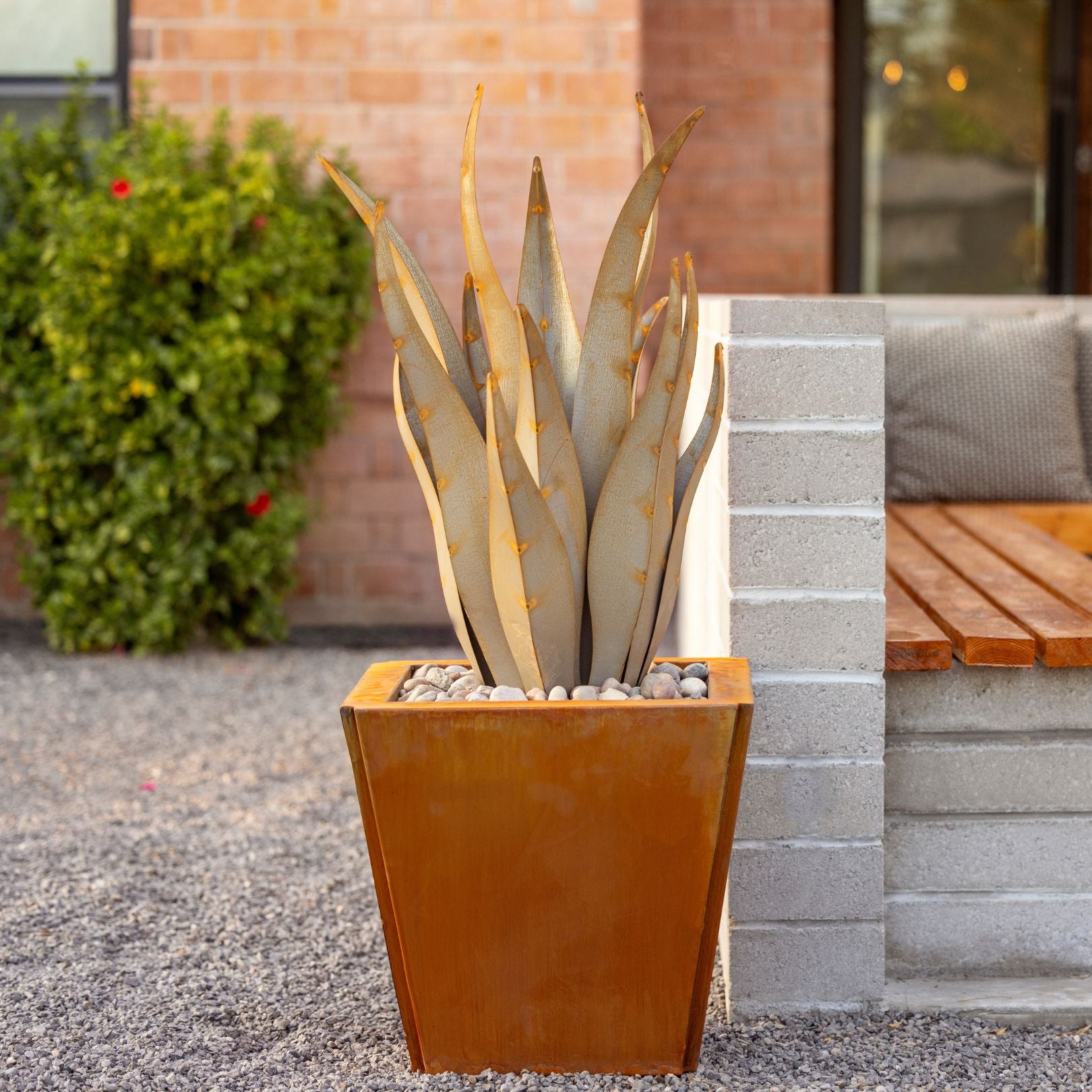 A metal emperor plant in a cabot planter. Featuring a residential real life landscape background.