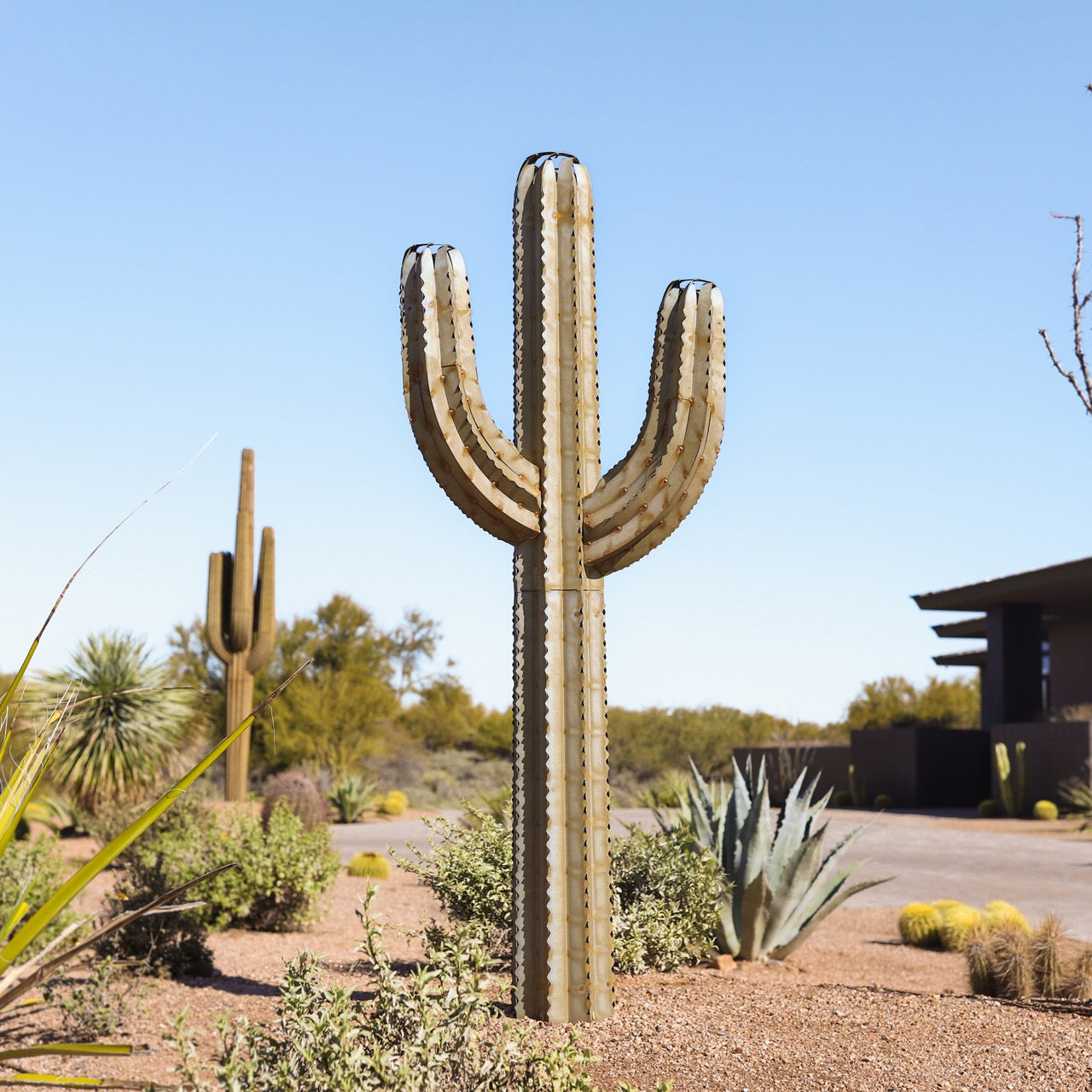 A metal saguaro cactus torch located in the desert. The sculpture's intricate design features a realistic saguaro body and arms, creating a lifelike appearance.