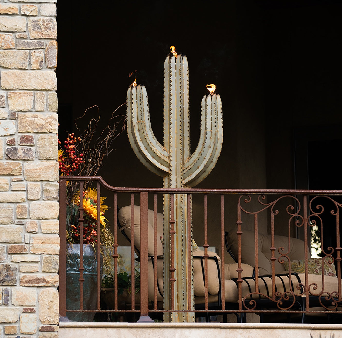 A metal saguaro cactus torch illuminated on a balcony. The sculpture's intricate design features a realistic saguaro body and arms, creating a lifelike appearance.