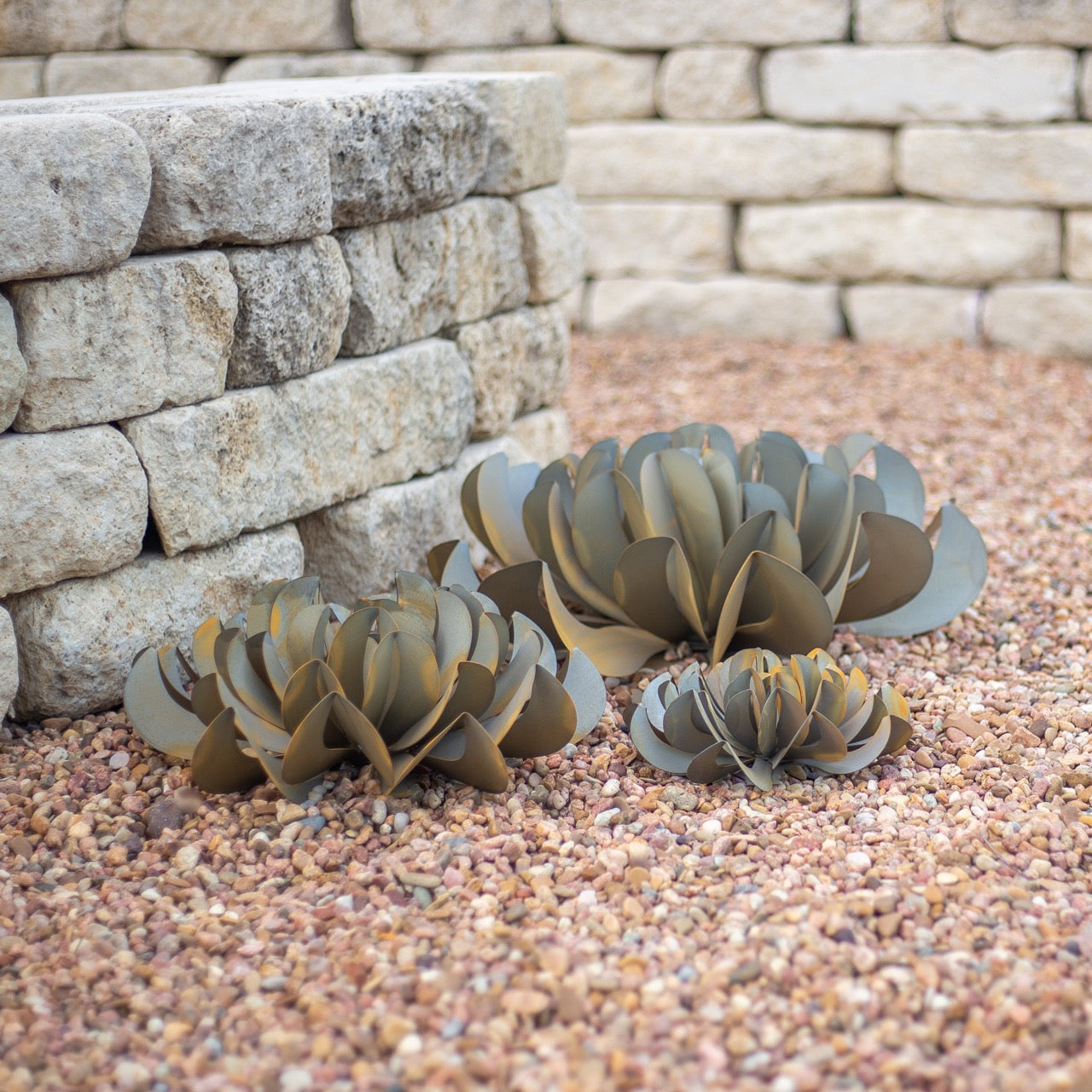 A group of small, medium, and large metal topsy turvy succulents, located outside next to a brick wall.