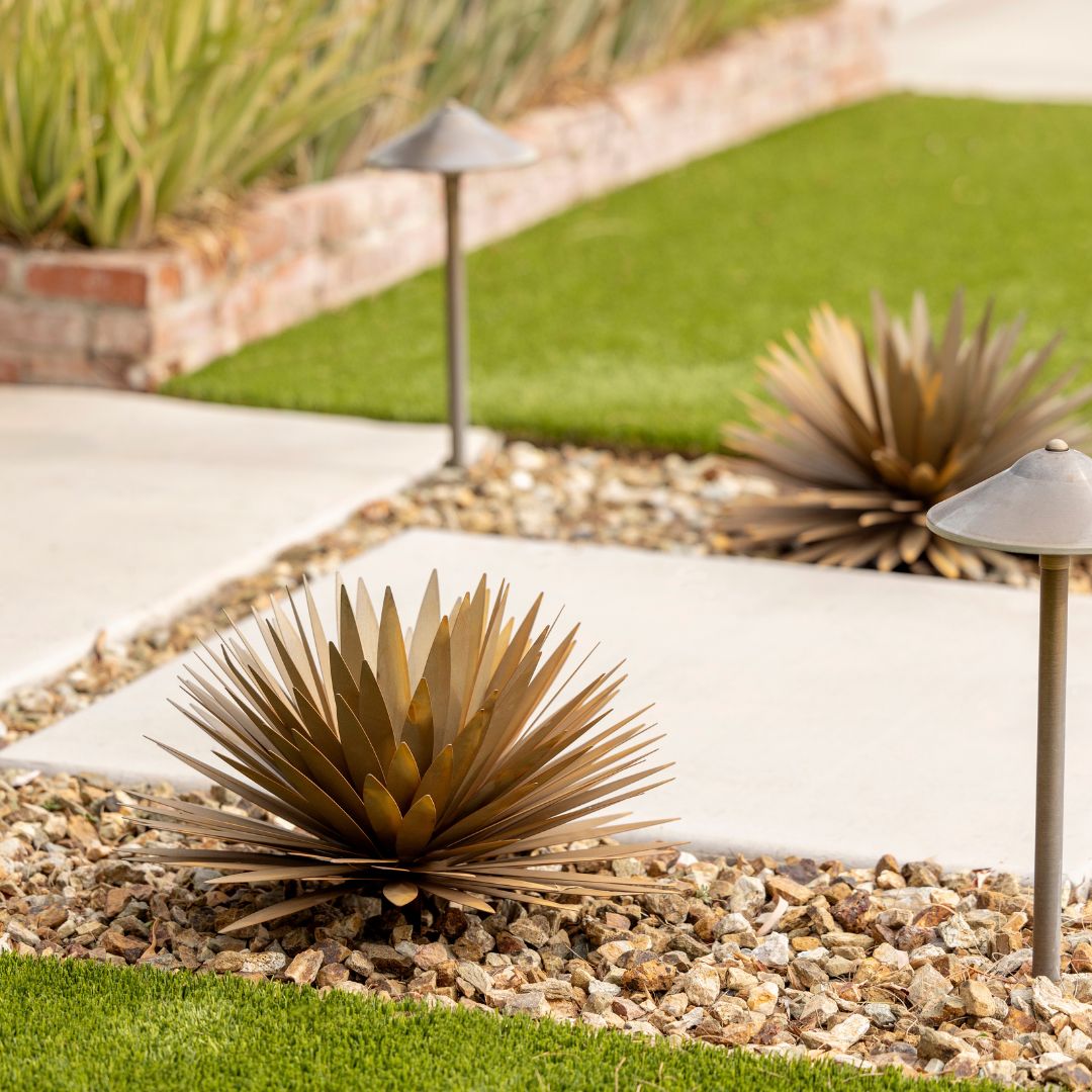 Two handcrafted realistic metal yucca succulents both sides of a pavement in the front yard of a house.